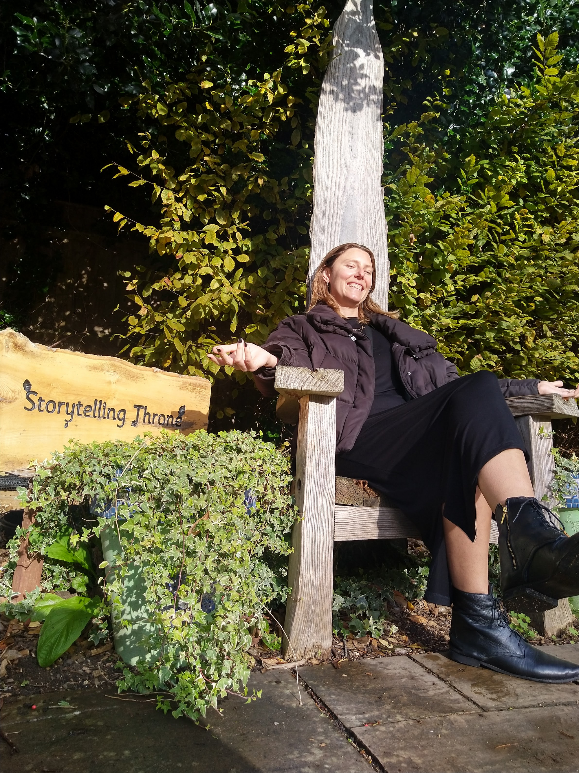 Sam sitting on a wooden throne with a sign next to it that says "Storytelling throne"