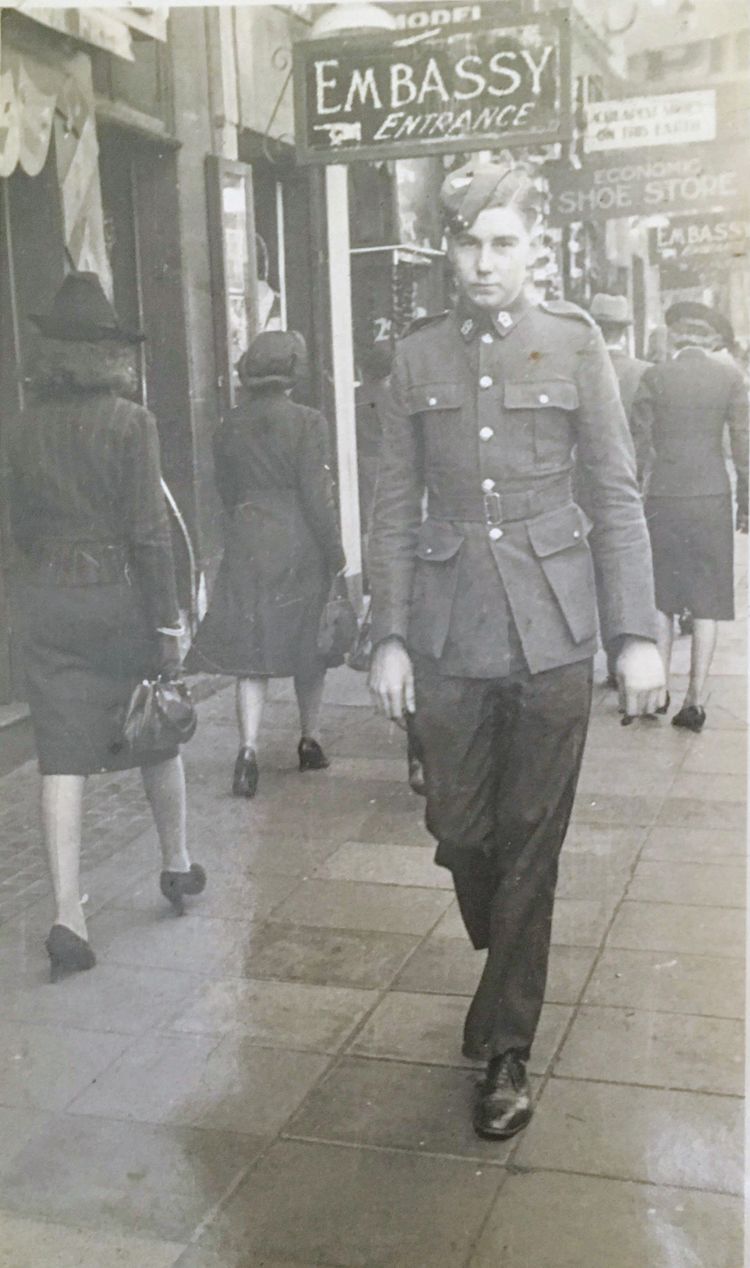 A photograph of a young soldier walking down a busy city street