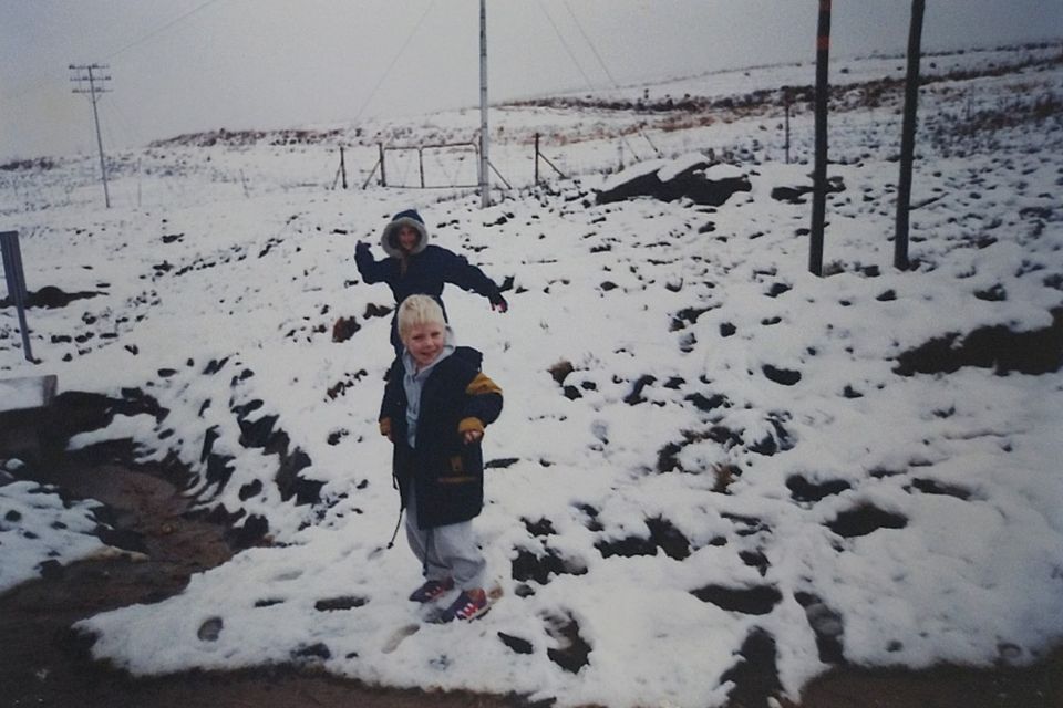 Two children standing in snow. The girl is about to throw a snowball at the boy, but he doesn't see it.